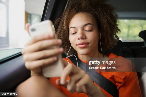 serene young woman listening to music with headphones and mp3 player in back seat of car - motorheadphones stock pictures, royalty-free photos & images