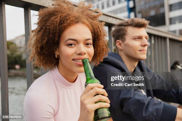 portrait young woman drinking beer on urban bridge - bier trinken stock-fotos und bilder