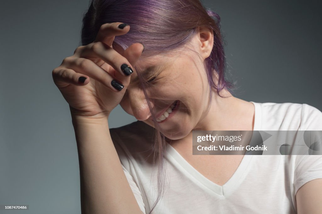 Young woman with dyed hair looking away and wincing against gray background