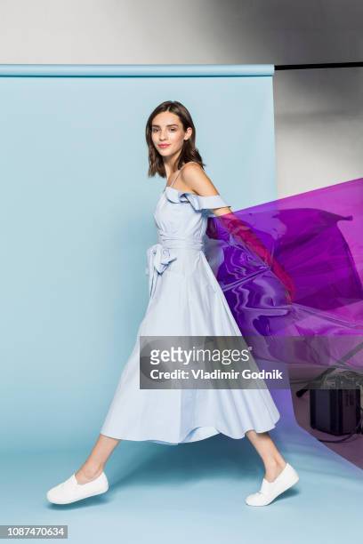 portrait of a female fashion model posing with purple plastic sheet against blue background - kleid stock-fotos und bilder