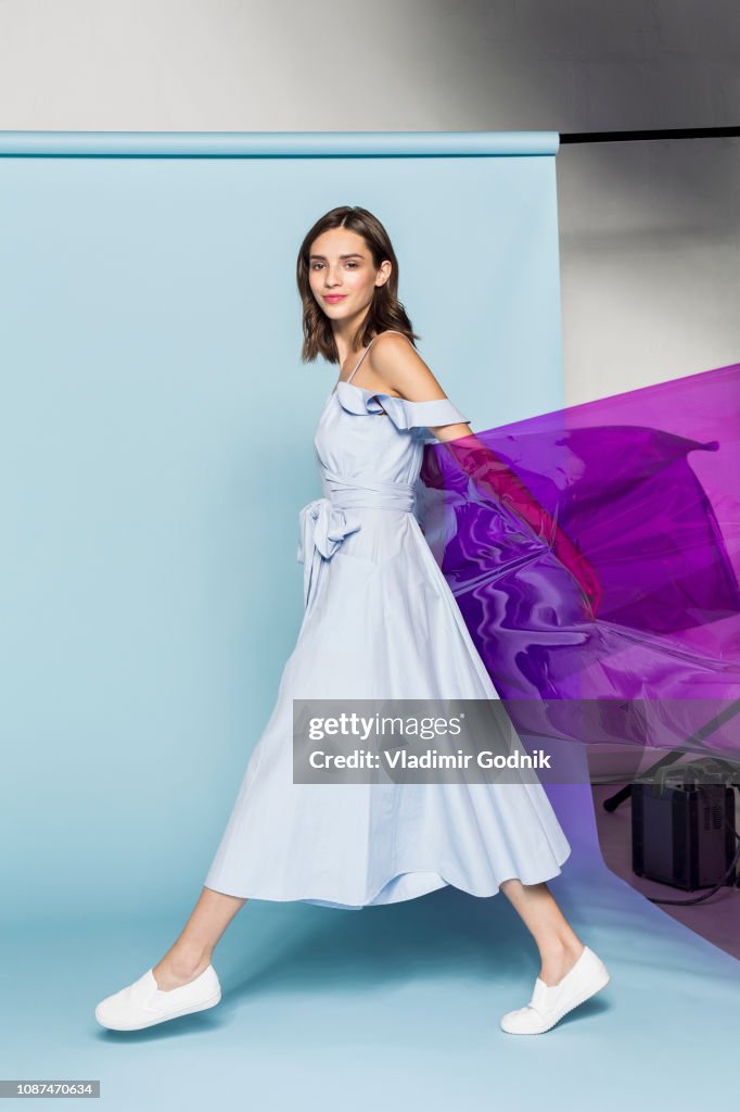 Portrait of a female fashion model posing with purple plastic sheet against blue background