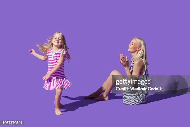 mother watching daughter dancing on purple background - blonde cheering stock-fotos und bilder