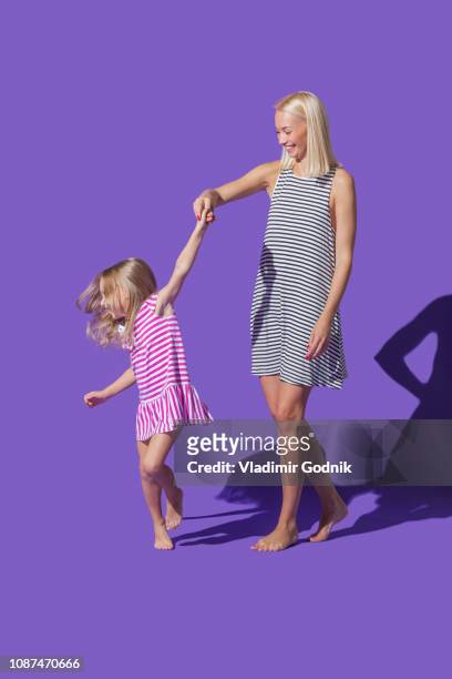 mother and daughter in striped dresses dancing on purple background - portrait studio purple background stock pictures, royalty-free photos & images
