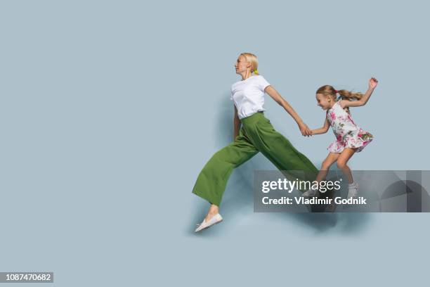 mother and daughter jumping against blue background - girl side view stockfoto's en -beelden