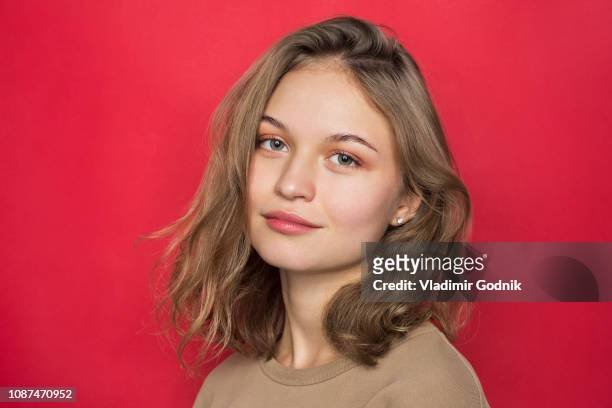 portrait of woman with light brown hair and smiling against red background - golvend haar stockfoto's en -beelden