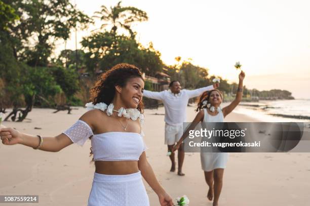 happy friends celebrating reveillon on the beach, running and holding white flowers. paraiso beach, mosqueiro - new year imagens e fotografias de stock