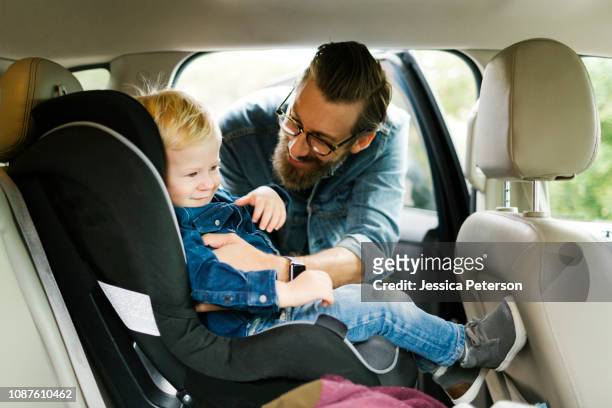 man putting his son into car seat - protect family stockfoto's en -beelden