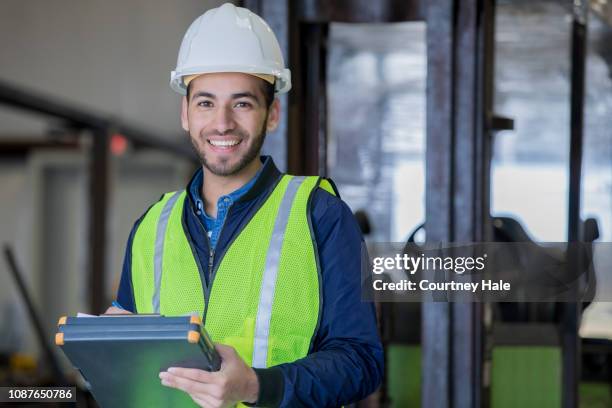 junge hispanic mann arbeitet als gabelstaplerfahrer im großlager lächeln beim tragen von schutzkleidung - gabelstapler amerika stock-fotos und bilder