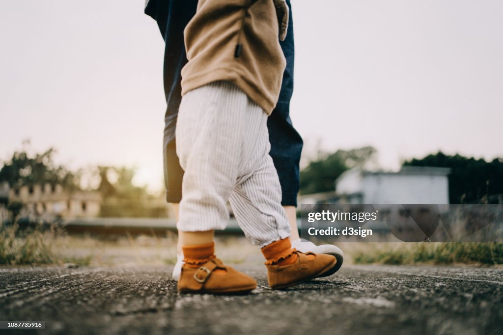 Close up low section of baby girl learning to walk with mother in park