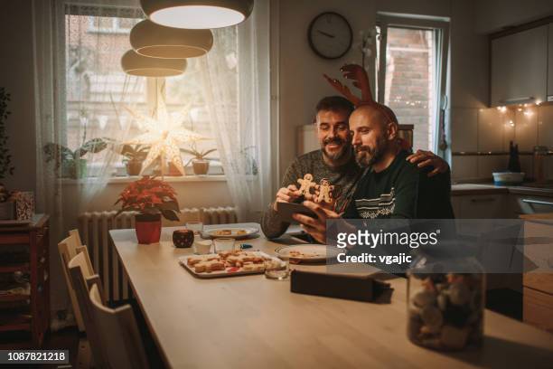 gay paar vieren kerst - couple at table with ipad stockfoto's en -beelden