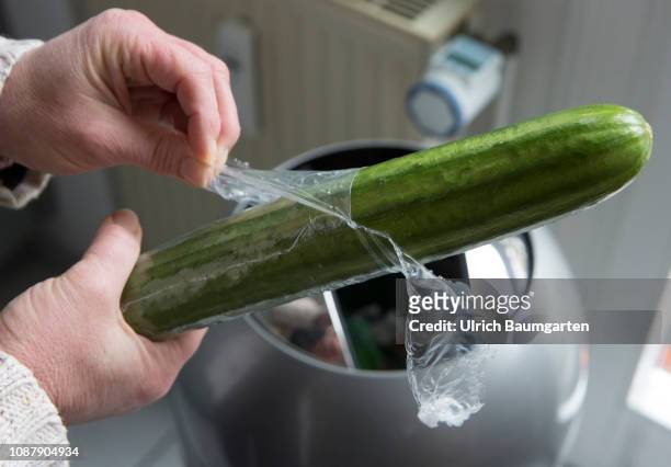 Without plastic packaging would be better! Hands take off the plastic packaging of a cucumber. .