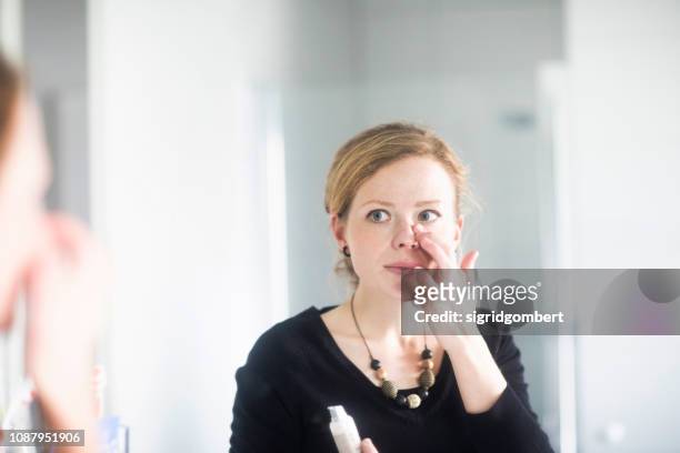 woman standing in bathroom applying make-up - concealer stock pictures, royalty-free photos & images
