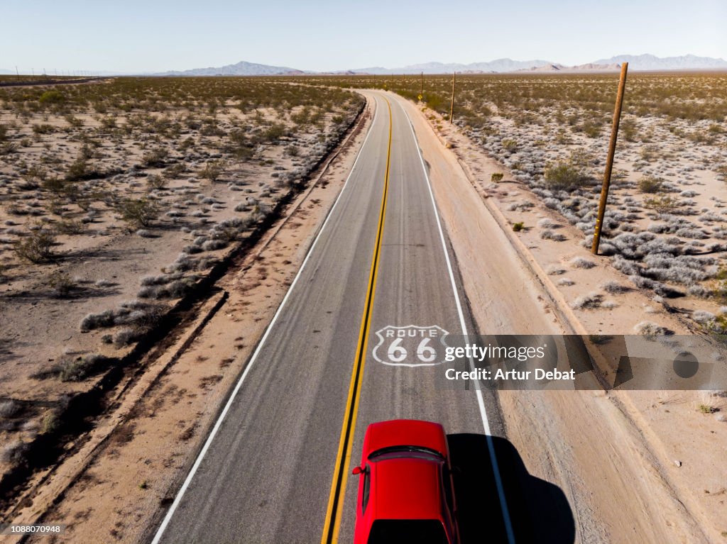 Drone view of American car driving in a straight road at the California desert.