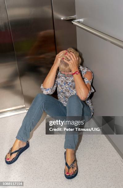 mature woman stuck in a lift. sits on the lift floor awaiting help & rescue - elevator trapped stock pictures, royalty-free photos & images