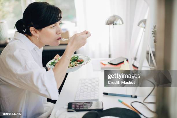 businesswoman eating pasta while looking at computer in home office. - telecommuting eating stock pictures, royalty-free photos & images