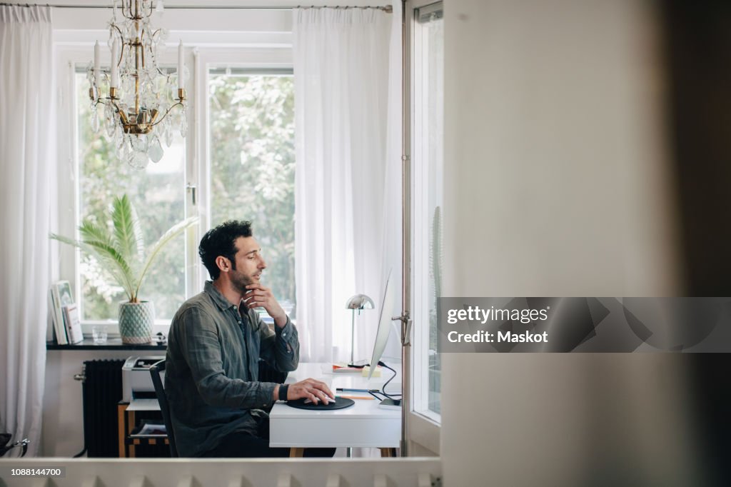 Serious young businessman using computer at desk in home office