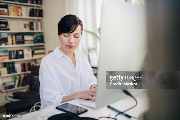 mid adult businesswoman looking at smart phone while using computer at desk - abgelenkt stock-fotos und bilder