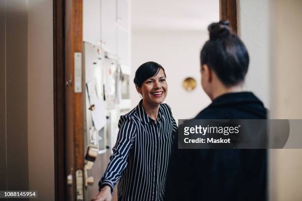 smiling businesswoman greeting coworker at doorway - entrée appartement photos et images de collection