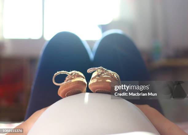 cute baby shoes on mother's pregnant tummy - babyshower stock-fotos und bilder