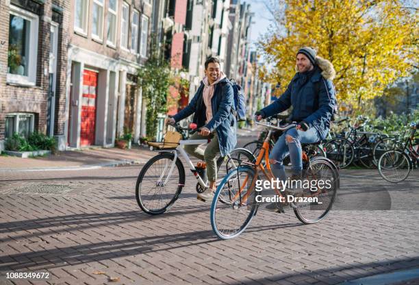 gay couple on rent-a-bikes - indonesian and european men are in relationship and spending time on city break - amsterdam cycling stock pictures, royalty-free photos & images