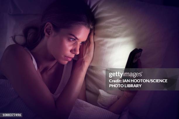 young woman looking at smartphone in bed - addiction stock pictures, royalty-free photos & images