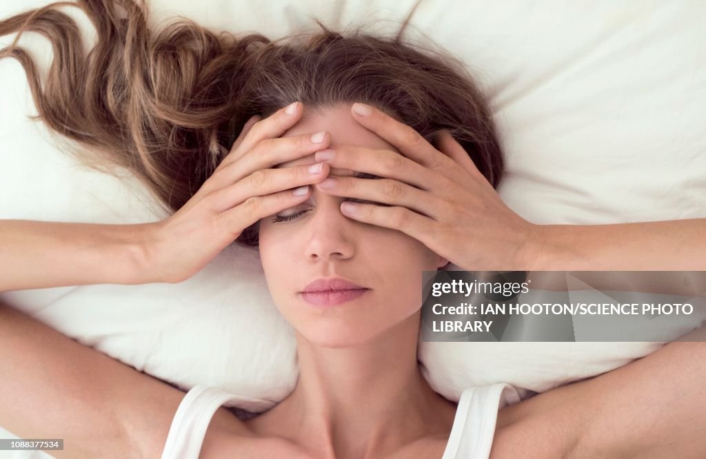 Young woman lying in bed and covering eyes