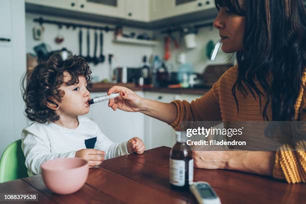 mother giving syrup to her son - cough medicine stock pictures, royalty-free photos & images