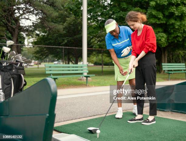 the active 77-years-old senior african-american woman teaching the 18-years-old caucasian girl to play golf. - golf lessons stock pictures, royalty-free photos & images