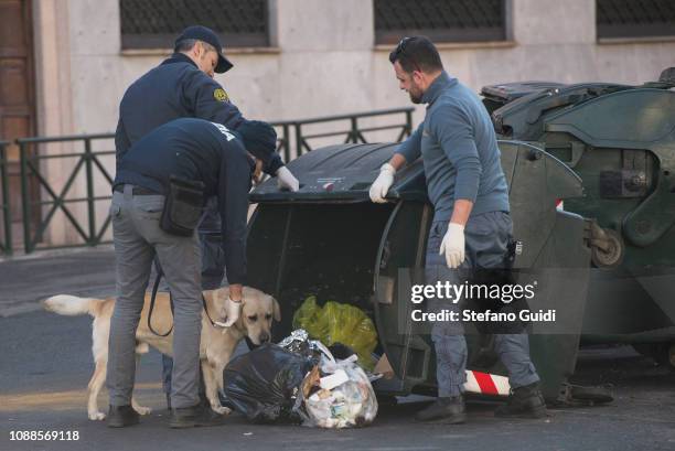 Three anti-explosive policemen and a anti-explosive dog approach a garbage can to check during a false alarm bomb package for a suspicious bag in...