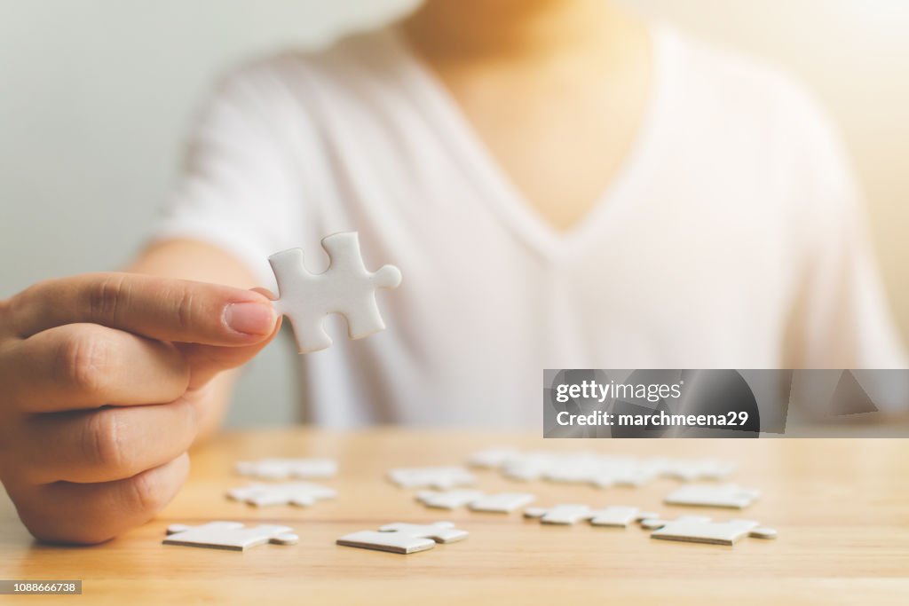 Mão de macho tentando conectar peças de branco quebra-cabeça na mesa de madeira. Cuidados de saúde para a doença de alzheimer, demência, perda de memória, consciência do autismo e conceito de saúde mental