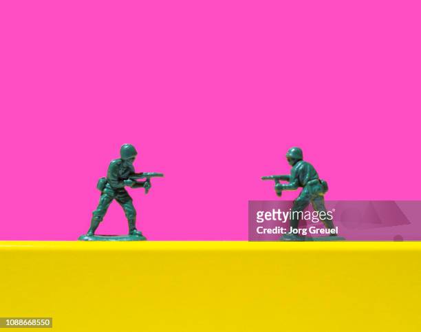 two toy soldiers pointing guns at each other - rivaliteit stockfoto's en -beelden