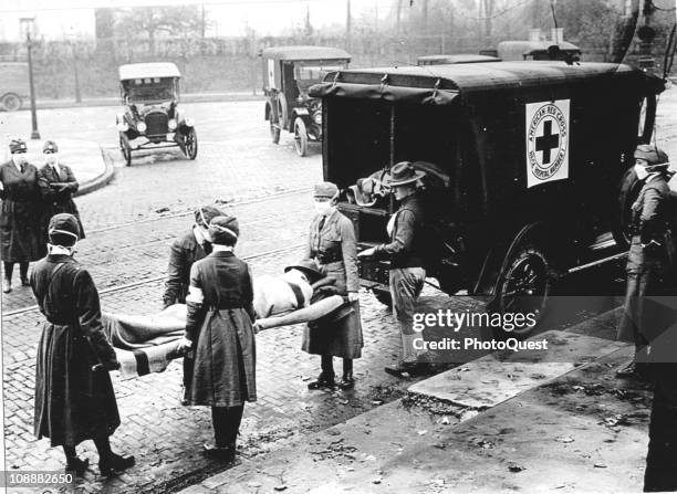 Members of the Red Cross Motor Corps, all wearing masks against the further spread of the influenza epidemic, carry a patient on a stretcher into...