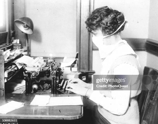 Typist wears mask while working at her office desk, during the influenza epidemic, 1918.