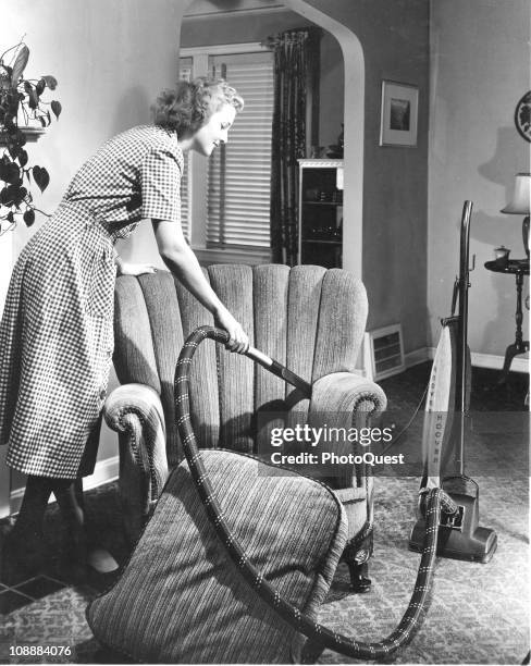 View of a woman using a Hoover vacuum cleaner to clean an armchair, 1950.