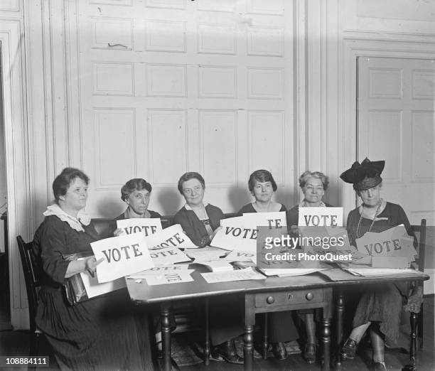 View of members of the National League of Women Voters, seated around a table, holding signs that read 'VOTE', September 1924.