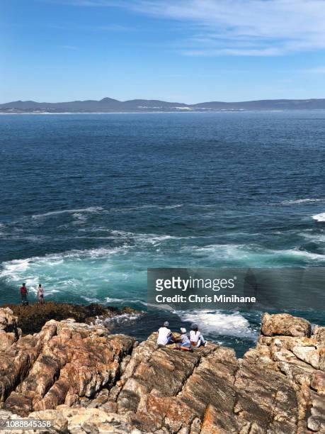 vertical beach shot of the cliffs in hermanus with people on the rocks during the whale festival cape town south africa - hermanus - fotografias e filmes do acervo