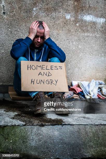 young homeless depressed man sitting outdoors holding cardboard sign - homeless winter stock pictures, royalty-free photos & images