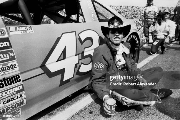Richard Petty, driver of the STP Pontiac, relaxes beside his race car at Daytona International Speedway just prior to the start of the 1985 Daytona...