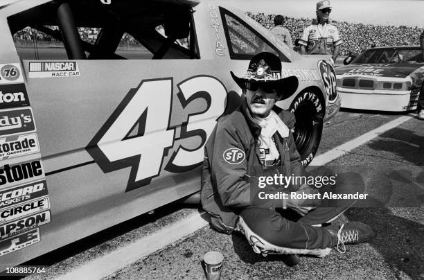 Richard Petty, driver of the STP Pontiac, sits beside his car at Daytona International Speedway just prior to the start of the 1985 Daytona 500...