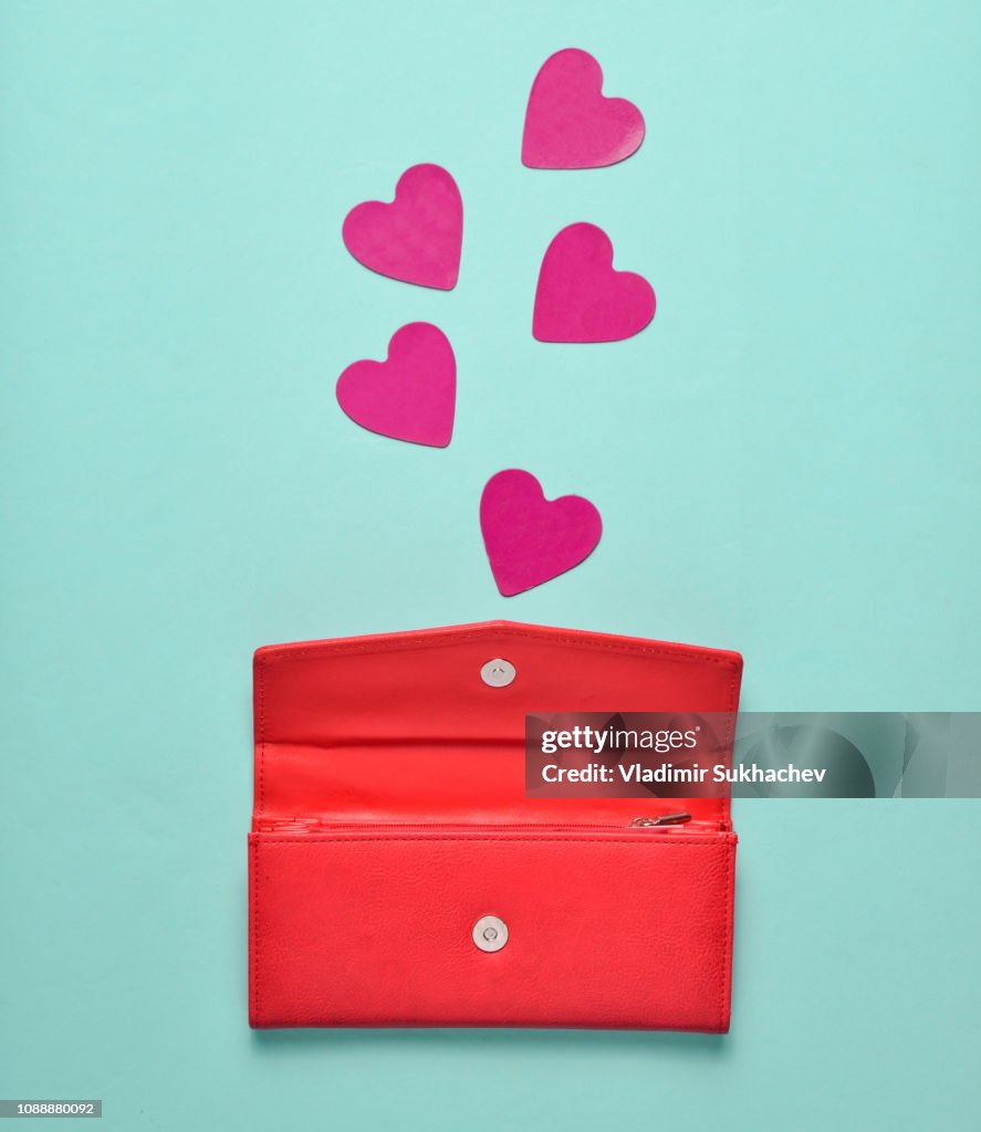 Red leather purse with decorative hearts on a blue pastel background, concept of love, minimalism