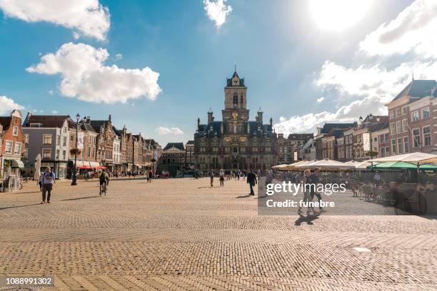 la piazza del mercato con il vecchio municipio sullo sfondo e ristoranti con terrazze piene di turisti a delft, nei paesi bassi - delft foto e immagini stock