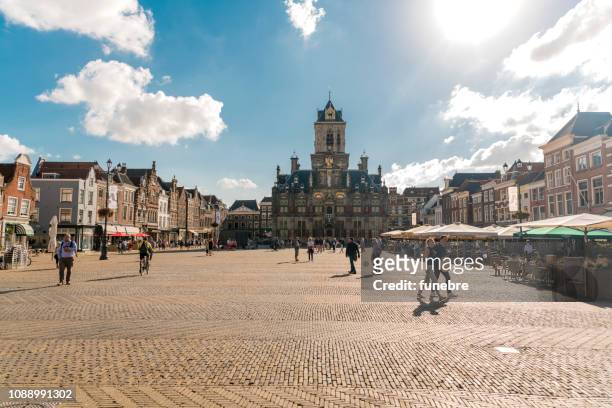 the market square with the old town hall in the background and restaurants with terraces full of tourists in delft, the netherlands - delft stock pictures, royalty-free photos & images