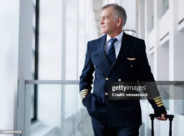 erfahrene senior pilot ziehen sein gepäck im flughafen terminal - aviatrice stock-fotos und bilder