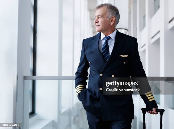 experienced senior pilot pulling his luggage in the airport terminal - airline pilot imagens e fotografias de stock