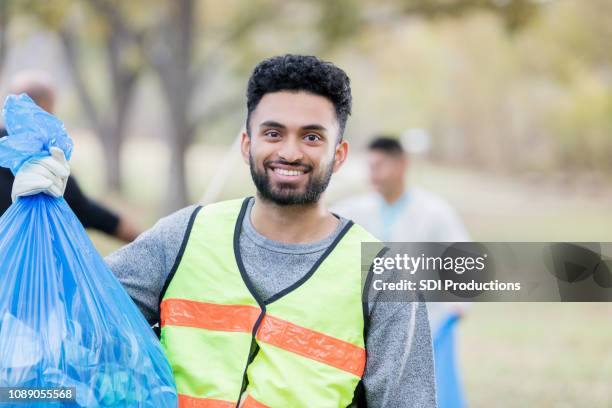 happy young man volunteers to cleanup community - picking up garbage stock pictures, royalty-free photos & images