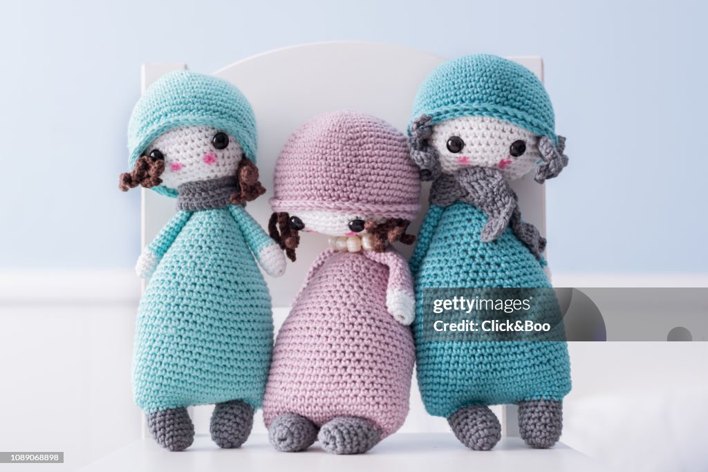 Three handmade crocheted dolls in blue with scarf and hat on a white chair.