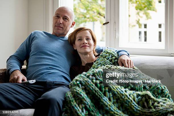 a mature couple relaxing on a sofa - watching tv at home stock pictures, royalty-free photos & images