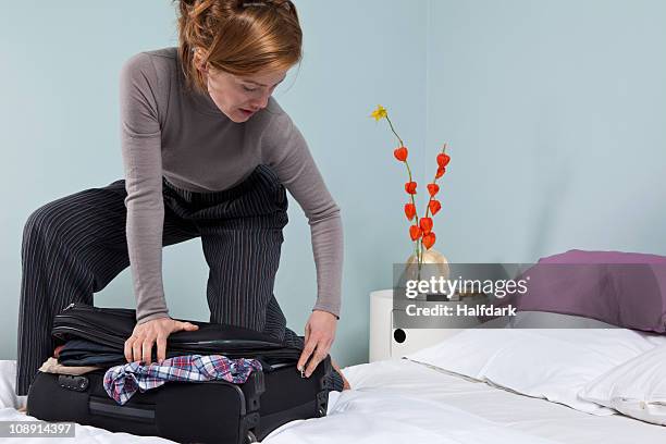 a woman trying to close an overflowing suitcase - suitcase close foto e immagini stock