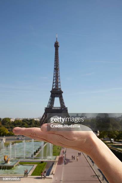 the optical illusion of a woman holding the eiffel tower in her hand, focus on hand - perspectiva forzada fotografías e imágenes de stock