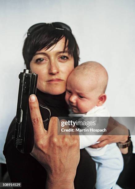 a mother holding a handgun up and a baby in her other arm - boy in hard hat stock-fotos und bilder